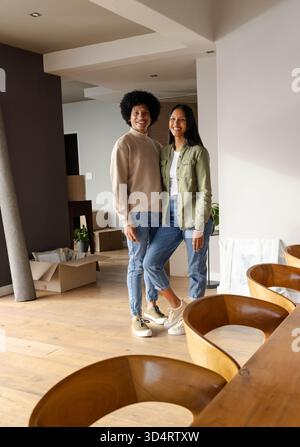 Lächelnde, vielfältige Paare stehen in einem modernen Essbereich mit Umzugskartons und Teppich Stockfoto