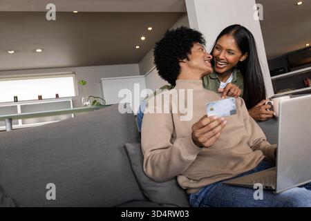 Stöbern Sie auf einem Laptop auf einem grauen Sofa im modernen Wohnzimmer mit Kreditkarte Stockfoto