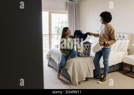 Diverse Klappkleidung für Paare auf Queensize-Bett im hellen Schlafzimmer, mit Wäschekorb und Kissen Stockfoto