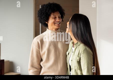 Ein lächelndes, vielfältiges Paar steht im Flur, mit Pappkartons und Holztür Stockfoto
