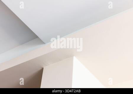 Eine ruhige Innenszene mit sich kreuzenden weißen und beigefarbenen Wänden mit scharfen Winkeln und sanften Schatten. Sauberes Design erinnert an modernen Minimalismus, Architekt Stockfoto