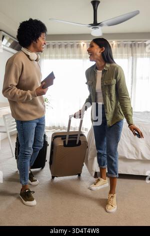 Plaudernder Mann und asiatische Inderin, die Pässe halten und Koffer im Hotelzimmer ziehen Stockfoto