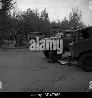 Ein archiviertes Schwarzweißfoto aus den 1970er Jahren zeigt eine Reihe von spezialisierten sowjetischen Lkws im Öllager Sloviansk, der ukrainischen SSR. Neben einem Geländefahrzeug GAZ-66 steht ein Feuerwehrwagen ZIL-131 mit großem Schaummonitor auf dem Dach. Diese Einsatzfahrzeuge sind in der Nähe der Tankstelle des Depots stationiert, die im Hintergrund sichtbar ist. Diese Szene verdeutlicht das hohe Maß an Sicherheitsvorsorge an der Industriestelle im friedlichen Donbass. Stockfoto