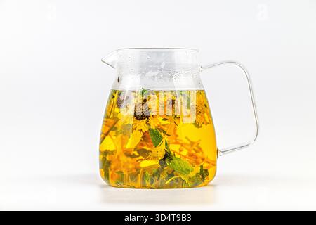 Ein Krug Tee mit Minzblättern darin. Der Pitcher ist klar und hat einen Griff. Der Tee ist gelb und hat einen minzigen Geschmack Stockfoto