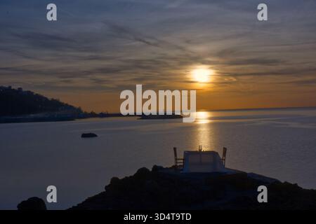 Ein intimer, wunderschön gedeckter Tisch, mit einer weißen Tischdecke überzogen und von zwei leeren Stühlen flankiert, sitzt auf einer zerklüfteten Klippe. Die Szene ist b Stockfoto