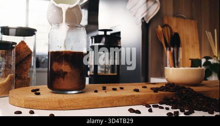 Gießen, Sahne und Eiskaffee in der Küche, Bohnen und Zutaten für Koffeingetränke, Milch oder Latte. Frühstück, kaltes Bier und Flüssigkeit mit Stockfoto