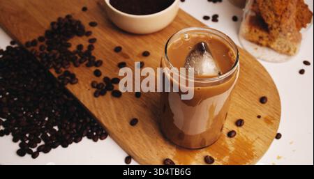 Eis, Kaffee und Getränk mit Glas auf dem Tisch in der Küche zu Hause für Koffeingetränk, Frühstück oder Morgengebräu. Cappuccino, kalter Latte und Zubereitung mit Stockfoto