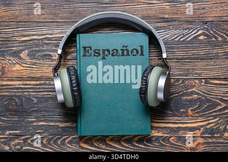 Buch und moderne Kopfhörer auf hölzernem Hintergrund. Konzept des Lernens Spanisch Stockfoto