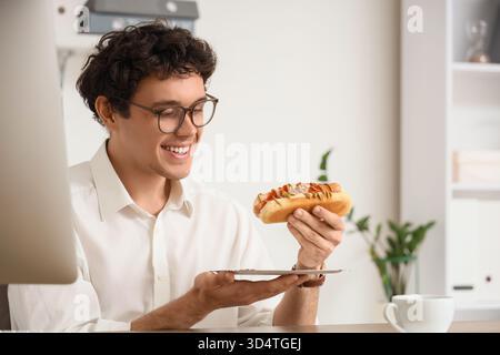 Junger Geschäftsmann mit leckerem Hotdog im Büro Stockfoto