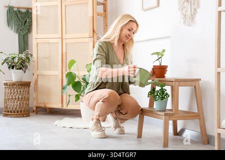 Reife blonde Frau, die zu Hause Pflanzen auf dem Stuhl tränkt Stockfoto