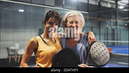 Padel, Sport und Porträt von Frauen auf dem Platz für Spiel, Spiel und Training für Herausforderungen. Indoor, fröhliche und reife Leute mit Schläger zum Workout Stockfoto