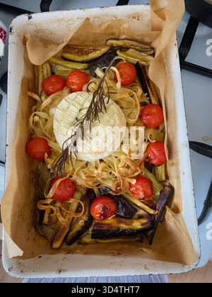 Gebackener Camembert-Käse ist wunderschön mit gerösteten Kirschtomaten, Nudelnestern und gebackenen Auberginen-Sticks auf Pergamentpapier, garniert mit Stockfoto