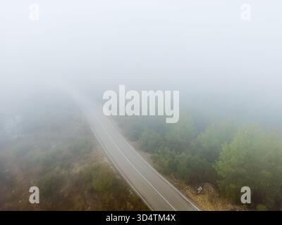Aus der Vogelperspektive einer leeren Bergstraße, die in Nebel verschwindet Stockfoto