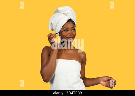 afroamerikanerin in Handtücher gewickelt, die Lidschatten aufträgt Stockfoto