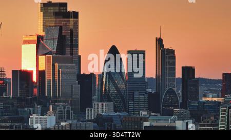 Großbritannien, London: Leuchtende warme Sonnenuntergangsfarben über Londons modernes Stadtbild, die legendäre Wolkenkratzer wie den Gherkin in einem atemberaubenden Panorama hervorheben. Drohnenflug Stockfoto