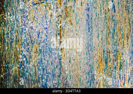 Nahaufnahme von irisierenden Lametta-Strängen, die in mehrschichtigen Metallic-Farben bei hellem Licht glitzern. Faszinierende Veranstaltungskulissen, sensorische Feiertagsvorstellungen Stockfoto