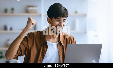 Mann, Der Tagsüber Erfolg Feiert, Während Er Das Notebook In Innenräumen Nutzt Stockfoto