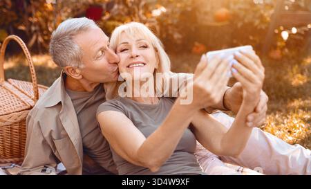 Senioren, die einen sonnigen Tag genießen, während sie ein Selfie in einem Park machen Stockfoto