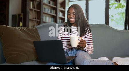 Frau genießt tagsüber Kaffee, während sie zu Hause an einem Laptop arbeitet Stockfoto