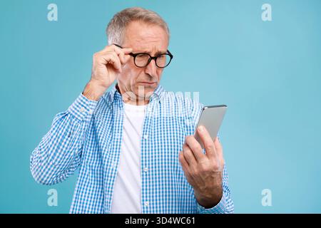 Ein reifer Mann sieht besorgt aus, als er schlechte Nachrichten auf dem Handy im Blue Studio liest Stockfoto