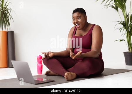 Übergewichtige afroamerikanische Frau genießt Video-Chat mit Yoga Coach auf Fitness Matte Stockfoto