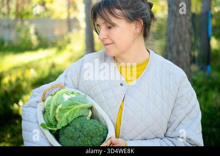 Lächelnde Farmerin, die Korb voll mit frischem Blumenkohl und Brokkoli hält. Erntezeit, einheimisches Gemüse, ballaststoffreiche Lebensmittel, saisonale Produkte und gesunde Gemüserezepte. Stockfoto