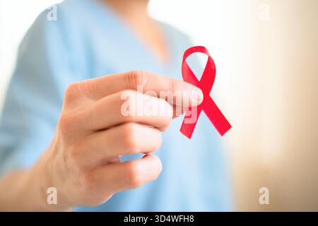 Äußerste Nahaufnahme der weiblichen Hand, die ein rotes Satin-Sensibilisierungsband hält, symbolisiert HIV-AIDS-Solidarität, Unterstützung und Hoffnung auf eine zukünftige Behandlung. Stockfoto