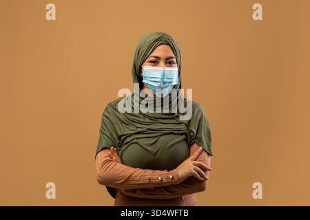 Junge muslimische Frau mit Hijab, die Schutzmaske trägt, posiert selbstbewusst im Studio-Setting Stockfoto