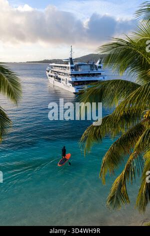 Yasawa-Inseln, Fidschi - 21. Oktober 2025: Aus der Vogelperspektive eines einsamen Paddleboarders, der über türkisfarbenes Wasser zu einem weit entfernten Kreuzfahrtschiff gleitet, eingerahmt von V Stockfoto