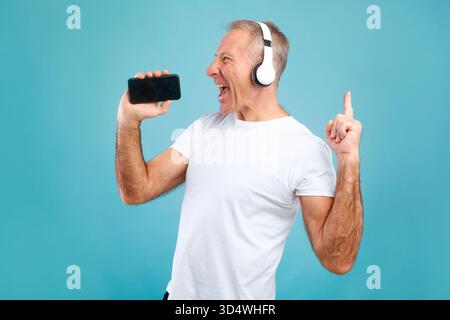 Reifer Mann singt gern mit Smartphone als Mikrofon in Carefree Dance Stockfoto
