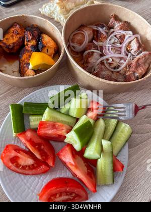 Köstliches gegrilltes Hühnchen- und Schweineschaschik serviert in umweltfreundlichen Schüsseln mit einem lebhaften Beilagensalat aus frischen Gurken und Tomaten, begleitet von Krieg Stockfoto