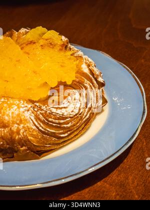 Köstliches goldbraunes dänisches Gebäck, das mit Puderzucker bestäubt ist, großzügig mit glänzenden kandierten Orangenscheiben belegt, serviert auf einem zarten hellen B Stockfoto