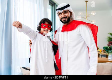 Familie aus dem Nahen Osten trägt traditionelle emiratische Kleidung und verbringt Zeit zu Hause zusammen. Arabischer Vater und Sohn lächelnd, in traditioneller Kleidung A Stockfoto