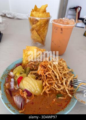 Köstliche Thai Khao Soi, eine nordthailändische Curry-Nudelsuppe, serviert mit knusprigen Nudeln, eingelegtem Kohl und roten Zwiebeln. Begleitet von knusprigem Wonton Stockfoto