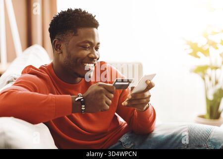 Ein lächelnder Mann macht Online-Shopping mit seinem Smartphone und seiner Kreditkarte Stockfoto
