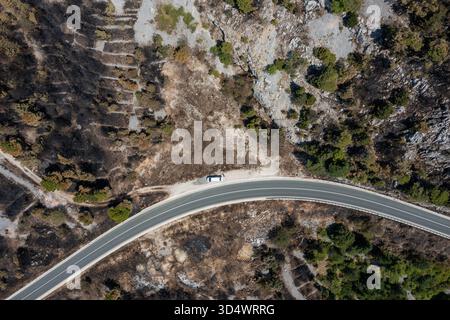 Aus der Vogelperspektive auf eine gewundene Straße, die durch die zerklüftete, felsige Landschaft führt, mit verbrannten Flecken, die sich von der lebhaften Grünfläche Biokovo, Repub abheben Stockfoto