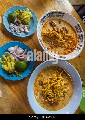 Geschmackvolle Nord-Thai-Khao Soi, eine traditionelle Curry-Nudelsuppe mit Huhn und knusprigen Nudeln, serviert mit frischer Limette, eingelegtem Senfgrün und Stockfoto