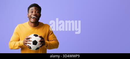 Junger Mann, der glücklich einen Fußball vor einem bunten Hintergrund hält Stockfoto