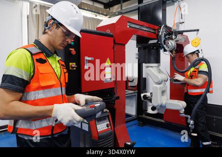 Ingenieur und Techniker, der mit dem industriellen Roboterarm in einem modernen Fabrikautomatisierungssystem arbeitet und Roboterschweißmaschine für intelligente Fertigung betreibt Stockfoto