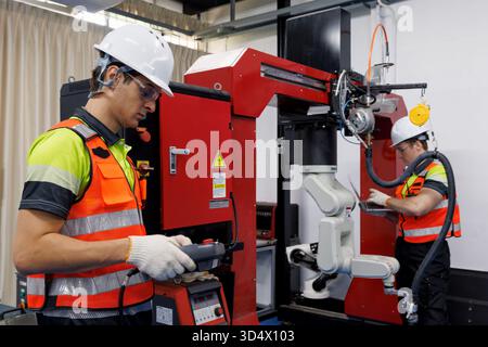 Ingenieur und Techniker, der mit dem industriellen Roboterarm in einem modernen Fabrikautomatisierungssystem arbeitet und Roboterschweißmaschine für intelligente Fertigung betreibt Stockfoto