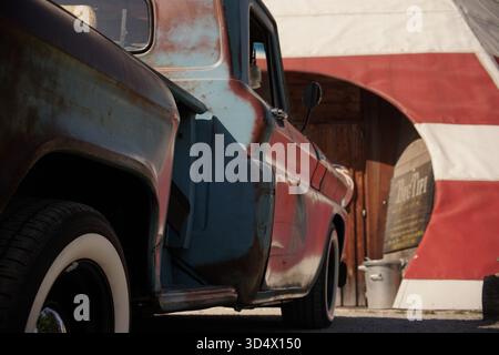 Rustikaler Vintage-Pickup-Truck, der neben einem zeltartigen Gebäude an einem Außenplatz geparkt wurde und verwitterte Farbe, Patina und Retro-Stil zeigt. Stockfoto