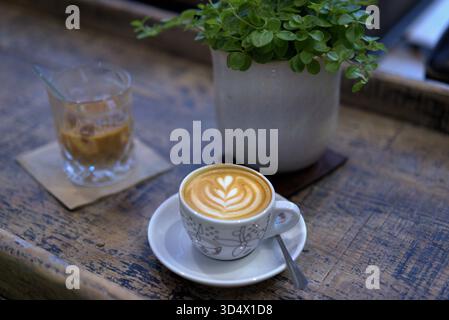 Cremige Latte Art in einem gemütlichen Café mit einem erfrischenden Glas Eiskaffee und einer kleinen Pflanze Stockfoto