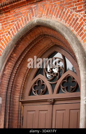 Bogenförmiger Eingang im gotischen Stil mit dekorativem Holztrakt und roter Ziegelfassade. Architektonische Details eines historischen Gebäudes. Stockfoto