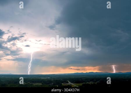 Blitze blitzen über den dunklen Himmel, während sich in der Dämmerung Gewitterwolken über fernen Bergen sammeln. Stockfoto