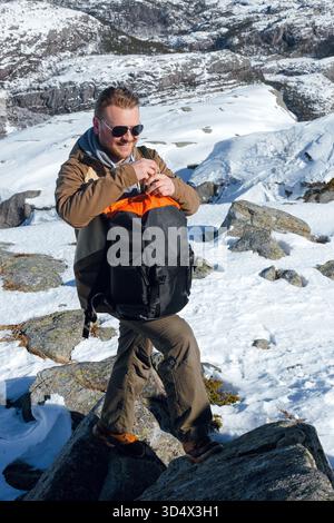 Mann in Sonnenbrille und Outdoor-Ausrüstung mit Rucksack in verschneiten Bergen. Preikestolen, Lysefjord in Norwegen Stockfoto