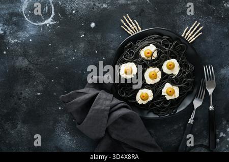 Halloween Party italienische schwarze Pasta dekorierte Horroroliven wie Augen auf schwarzem Teller auf alten dunklen Tisch Hintergrund. Monstergesicht aus Pasta. Halloween Deko und Halloween Food Konzept. Mock-Up. Stockfoto