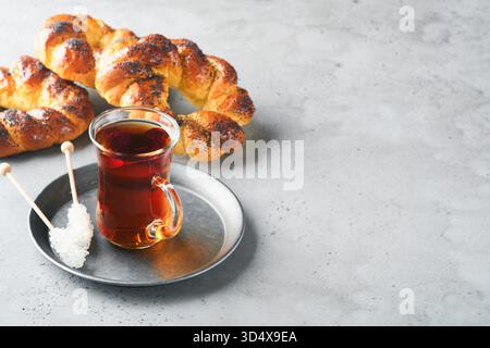 Türkischer schwarzer Tee. Eine Glasschale türkischer schwarzer Tee und knuspriger türkischer traditioneller Bagel auf grauem Betontischhintergrund. Frühstücksgebäck-Konzept. Traditionelles türkisches Heißgetränk. Stockfoto