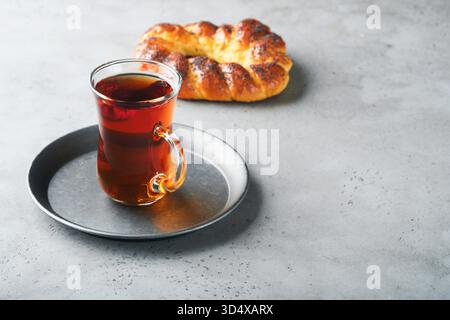 Türkischer schwarzer Tee. Eine Glasschale türkischer schwarzer Tee und knuspriger türkischer traditioneller Bagel auf grauem Betontischhintergrund. Frühstücksgebäck-Konzept. Traditionelles türkisches Heißgetränk. Stockfoto