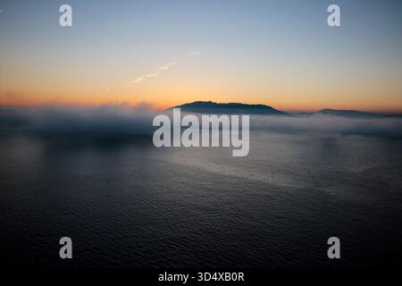 Tanger, Marokko. November 2025. Eine dichte Nebelbank erstreckt sich flach über die marokkanische Küste in der Nähe der Straße von Gibraltar in der Abenddämmerung, wobei Berggipfel über der Nebelschicht auftauchen. Das lokale Phänomen, das typisch ist, wenn warme, feuchte Luft aus dem Atlantik über kühlere Küstengewässer strömt. Quelle: Kevin Izorce/Alamy Live News Stockfoto