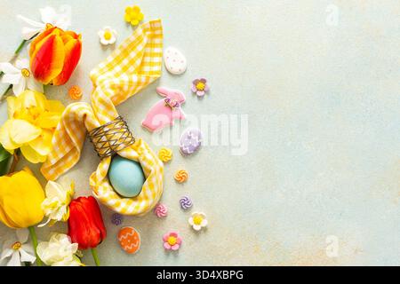 Helle Frühlingsblumen umgeben einen wunderschön gedeckten Tisch mit pastellfarbenen Ostereiern, Süßigkeiten und dekorativen Elementen, die den Geist der Urlaubsatmosphäre einfangen. Stockfoto